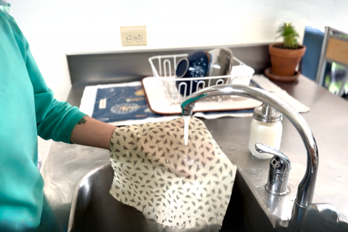 Kitchen, sink, metal surfaces. A person is in action of washing bee pattern beeswax food wrap.